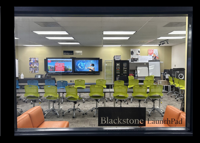 Modern classroom with green chairs, screens, and orange couches.