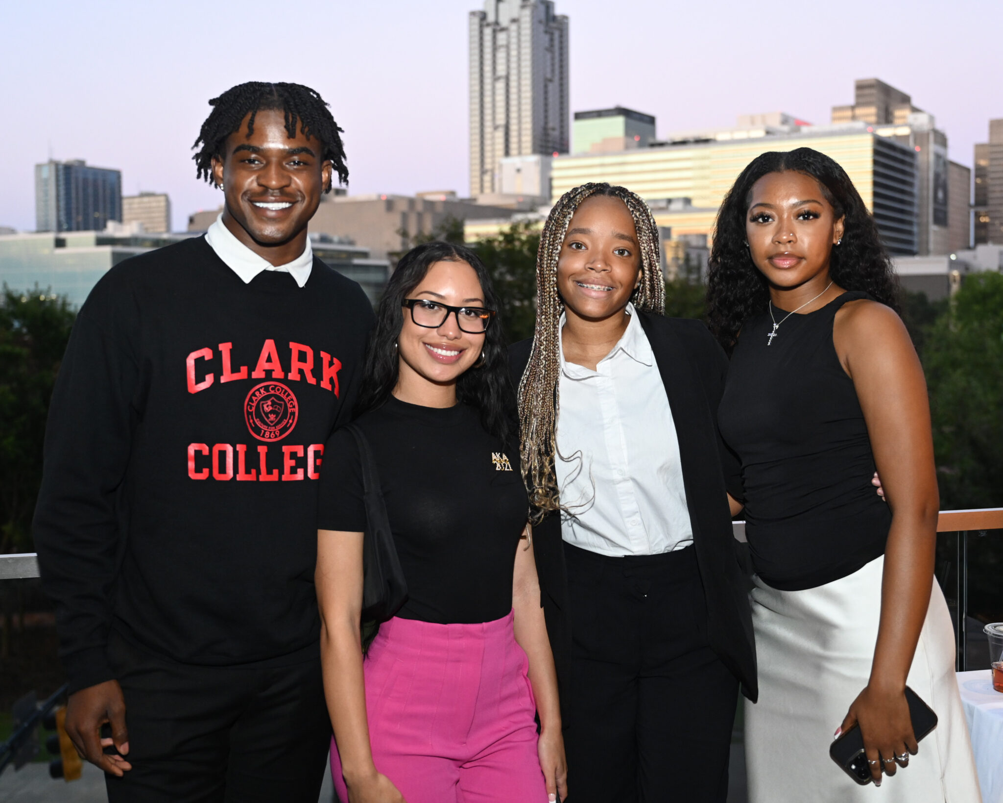 Four smiling people standing together with a city skyline in the background.