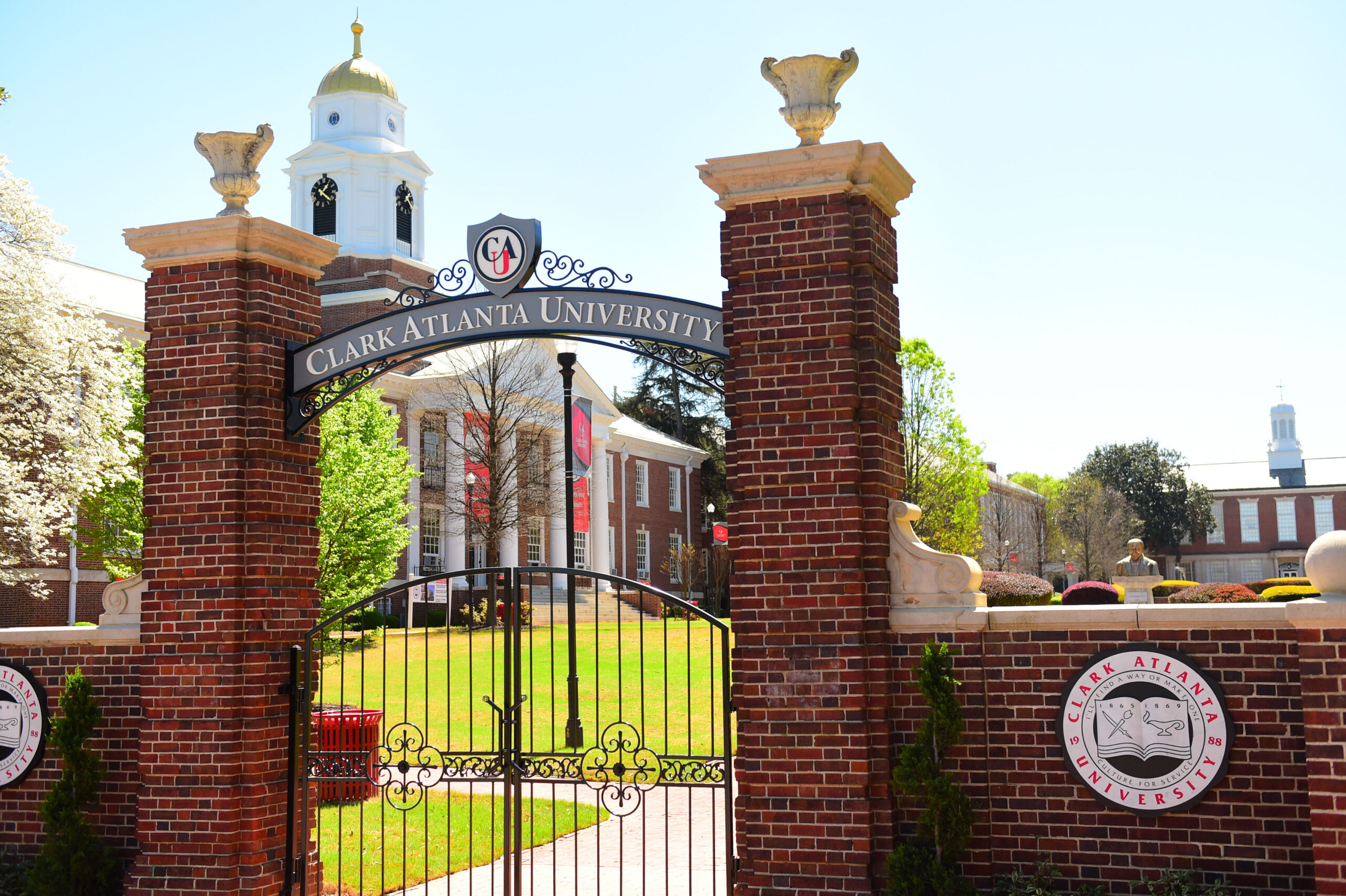 Brick university gate with arch and distant building.