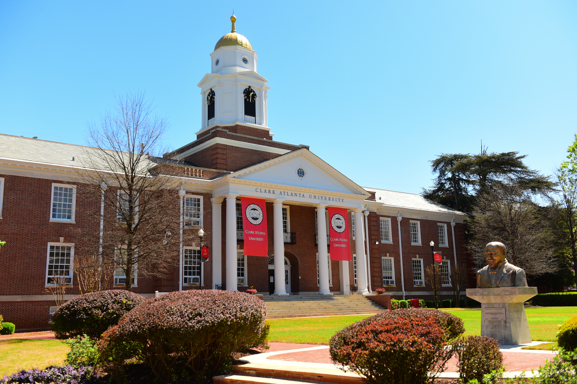 Red-brick building with a white dome and banners, surrounded by a manicured lawn.