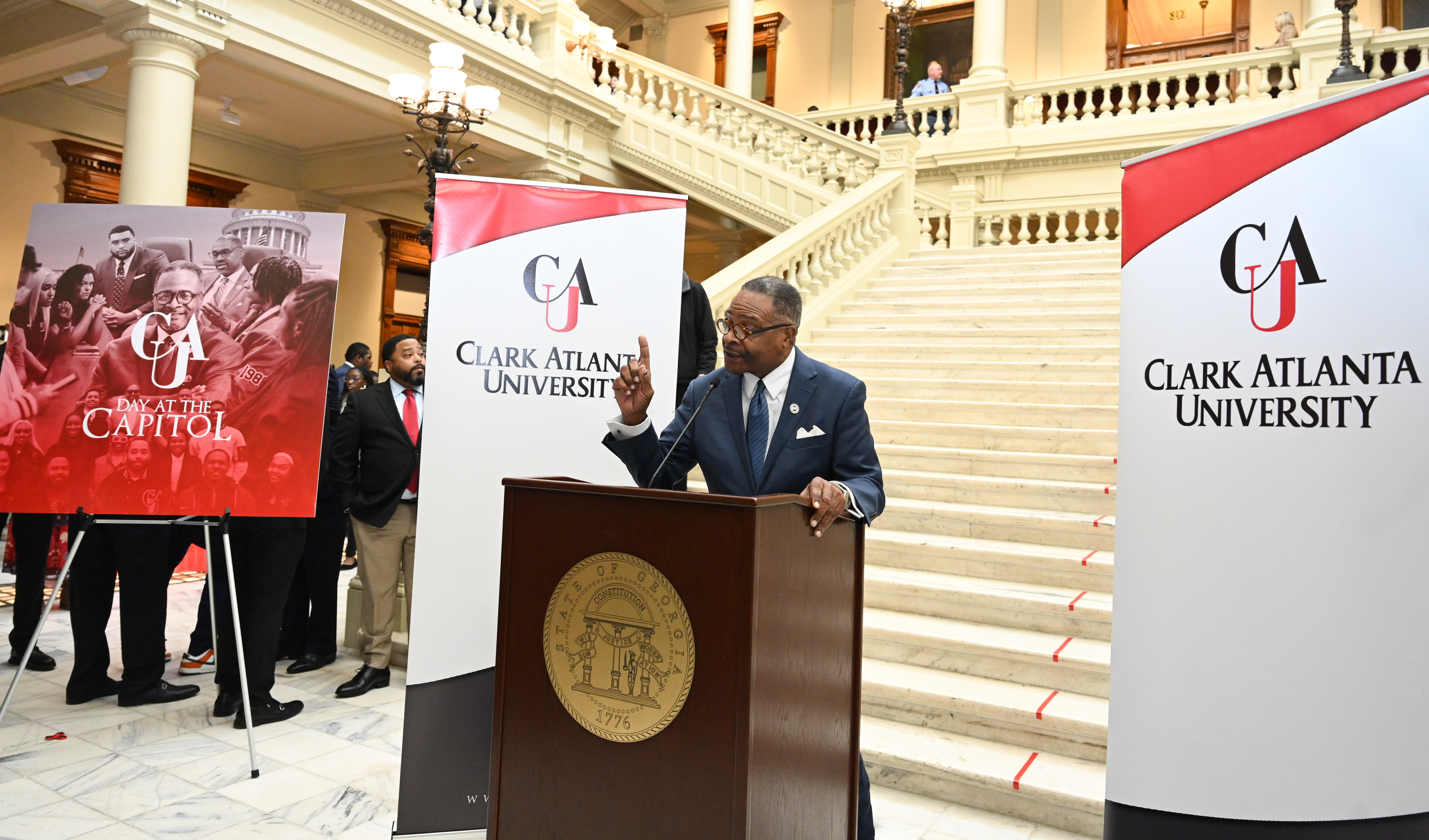 Speaker at podium, Clark Atlanta University banners, grand staircase in the background.
