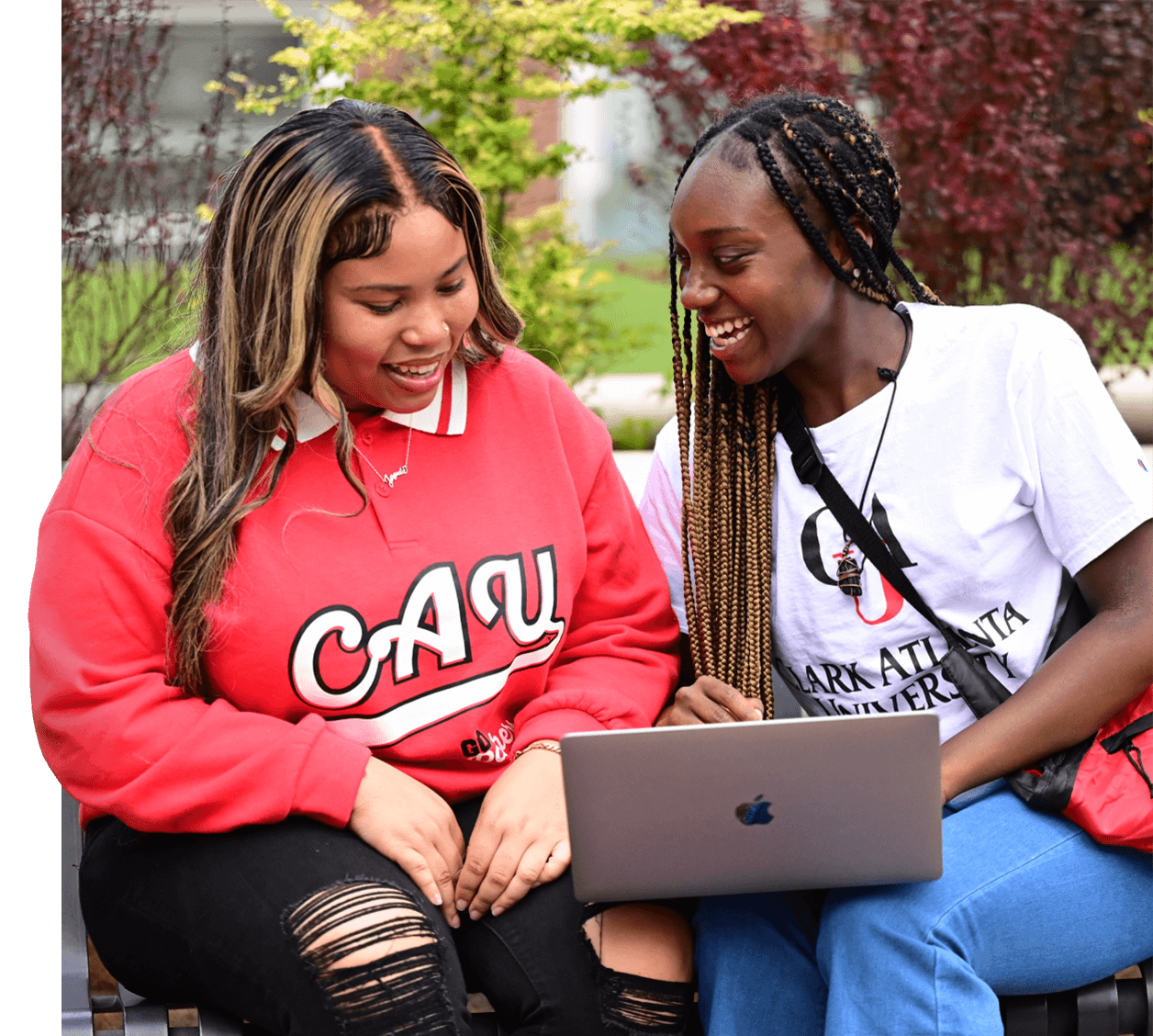 Two young women smiling and looking at a laptop outside.