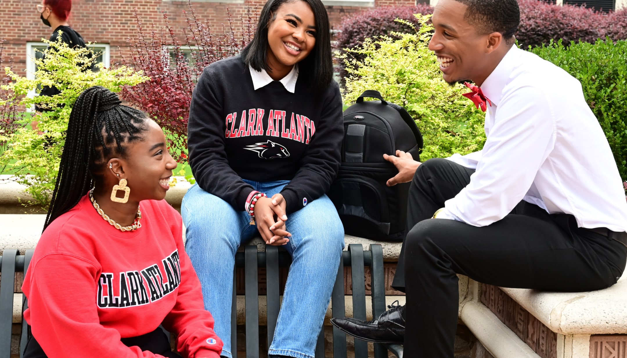 Three students in casual attire smiling and talking outdoors.