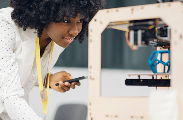Woman observing a 3D printer model with curiosity, holding a phone.