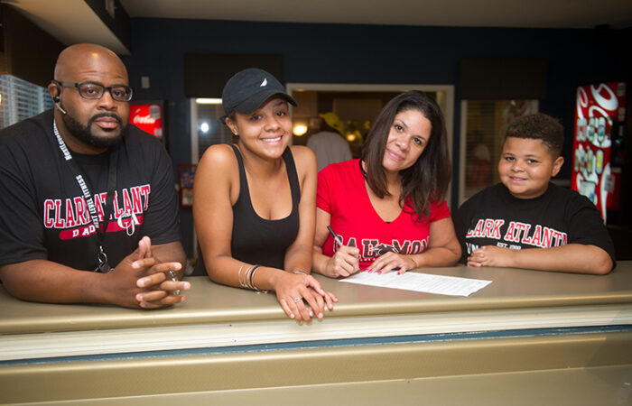 Four people wearing CAU gear, smiling, and sitting at a table with a document.