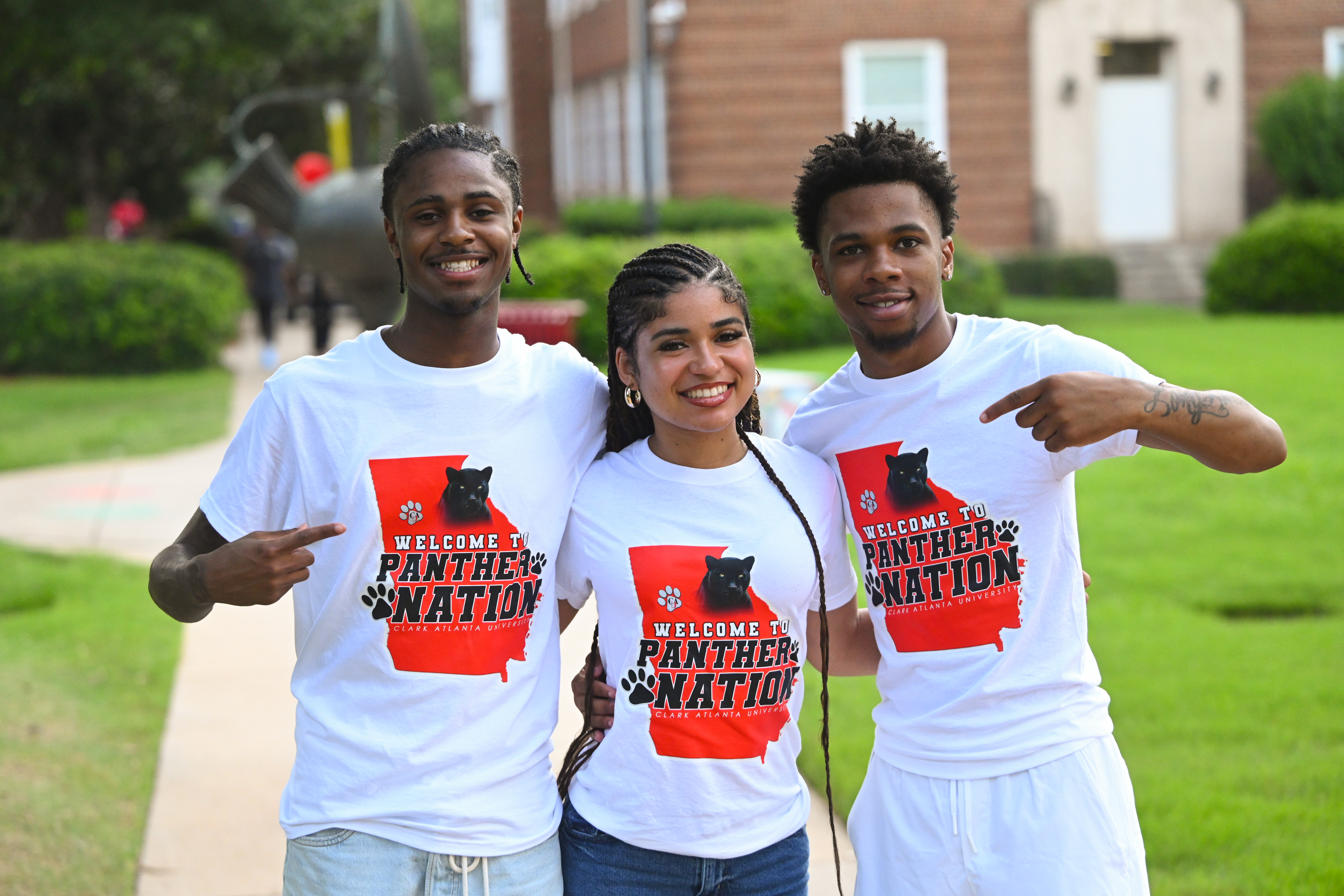 Three people smiling outdoors, wearing matching white T-shirts.