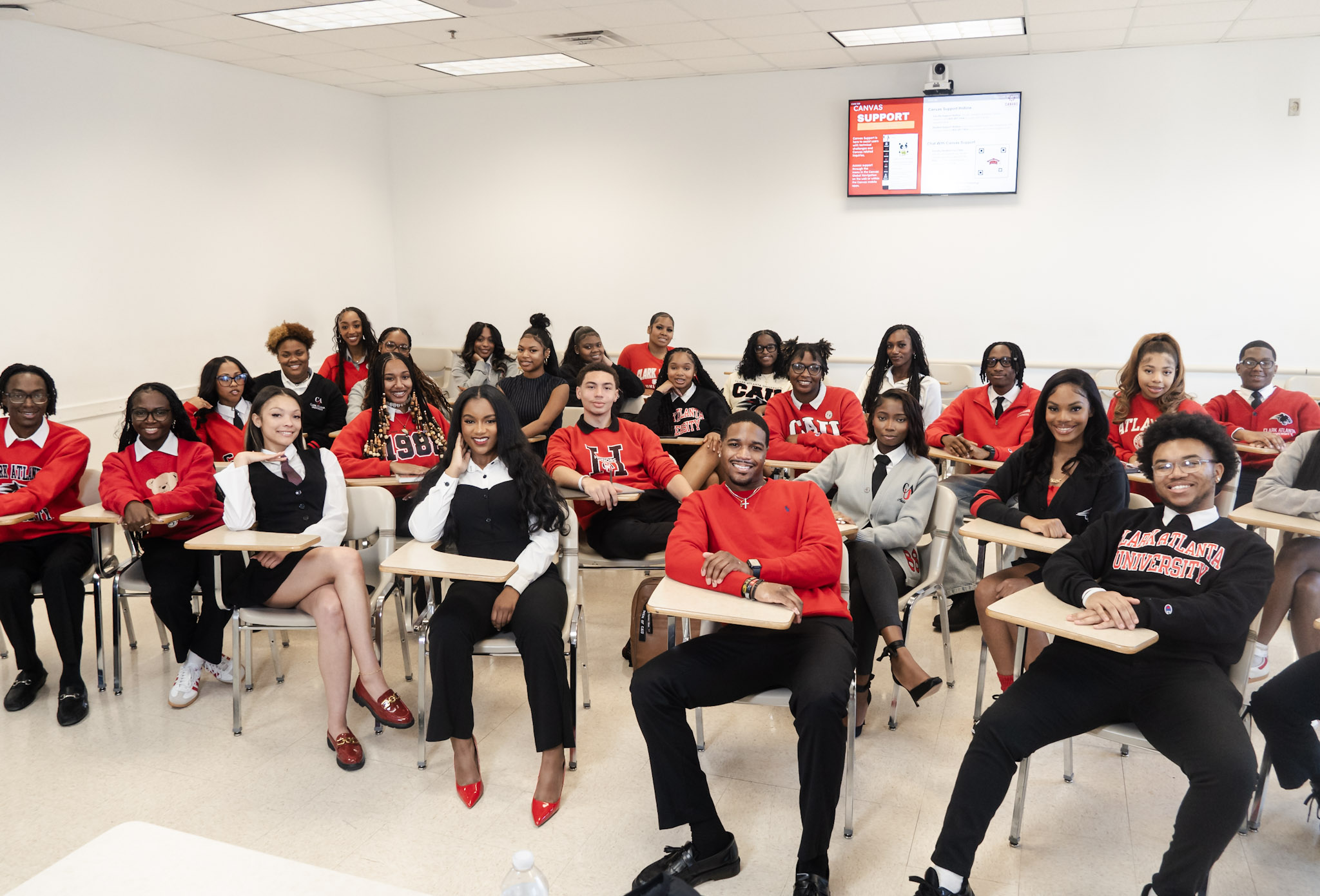 Classroom with smiling students wearing red and black, seated at desks.