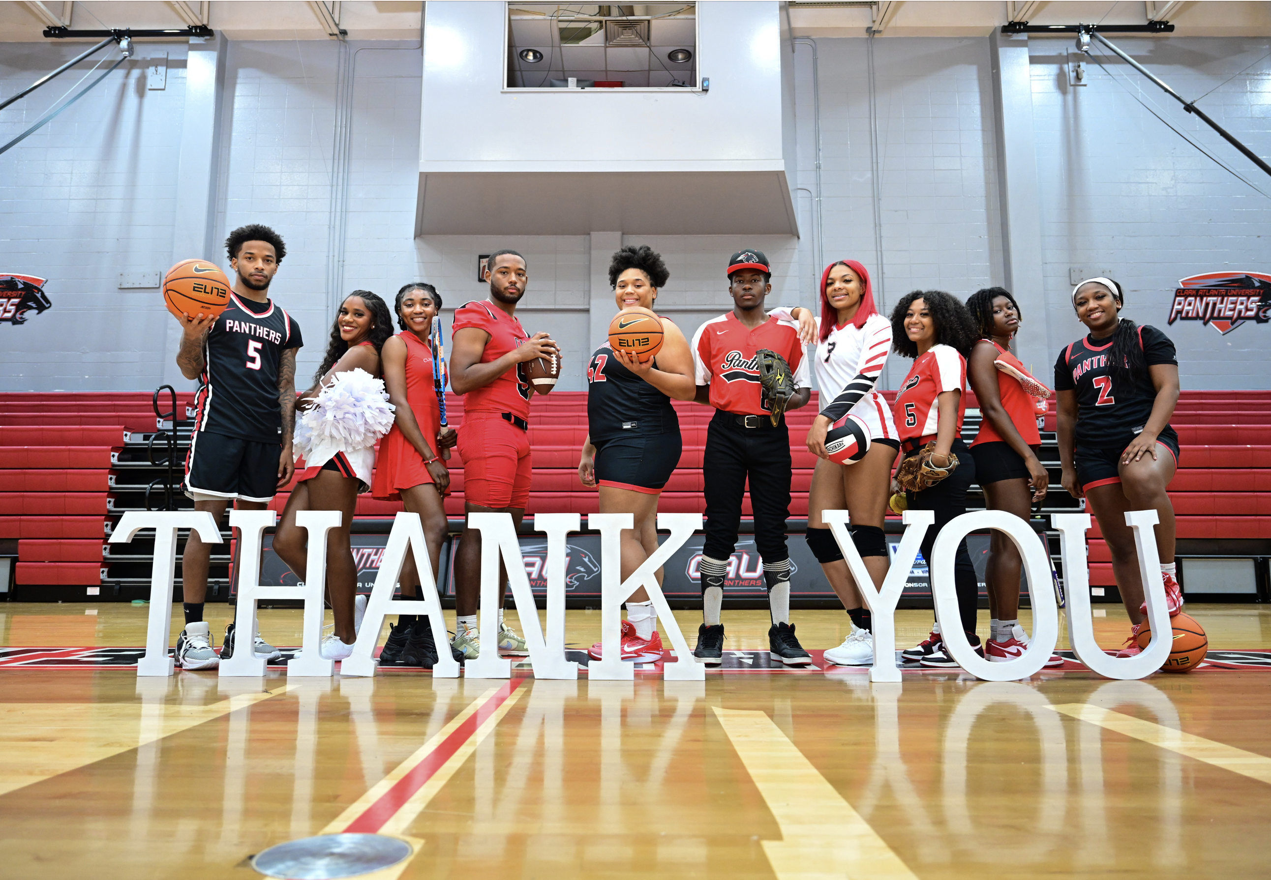 Basketball team posing in gym behind large "THANK YOU" letters.
