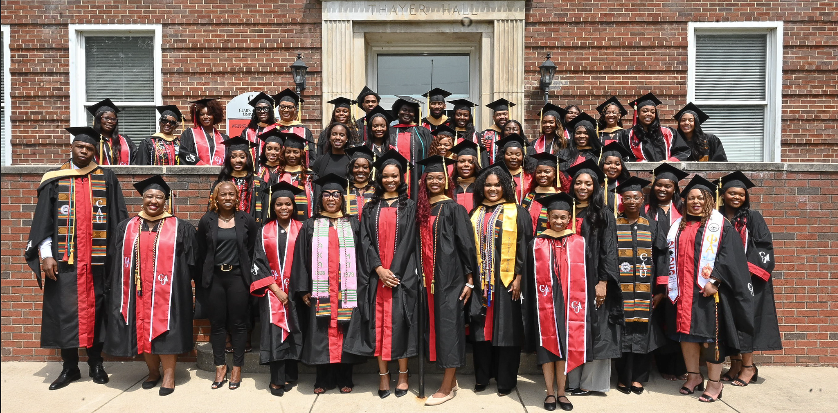 Graduates in caps and gowns pose in front of a brick building.