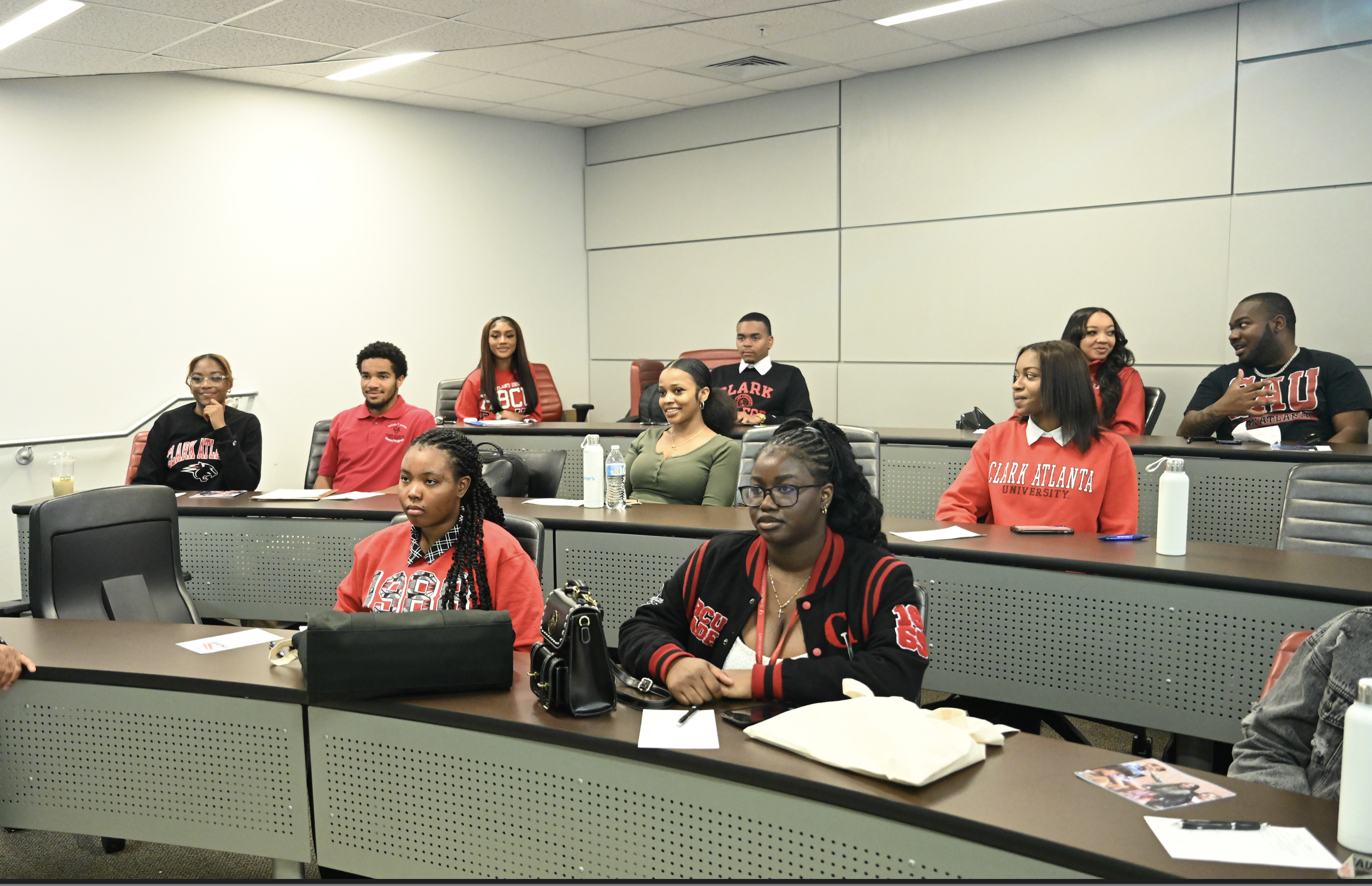 Students in a classroom, wearing red and black attire, sitting attentively at desks.