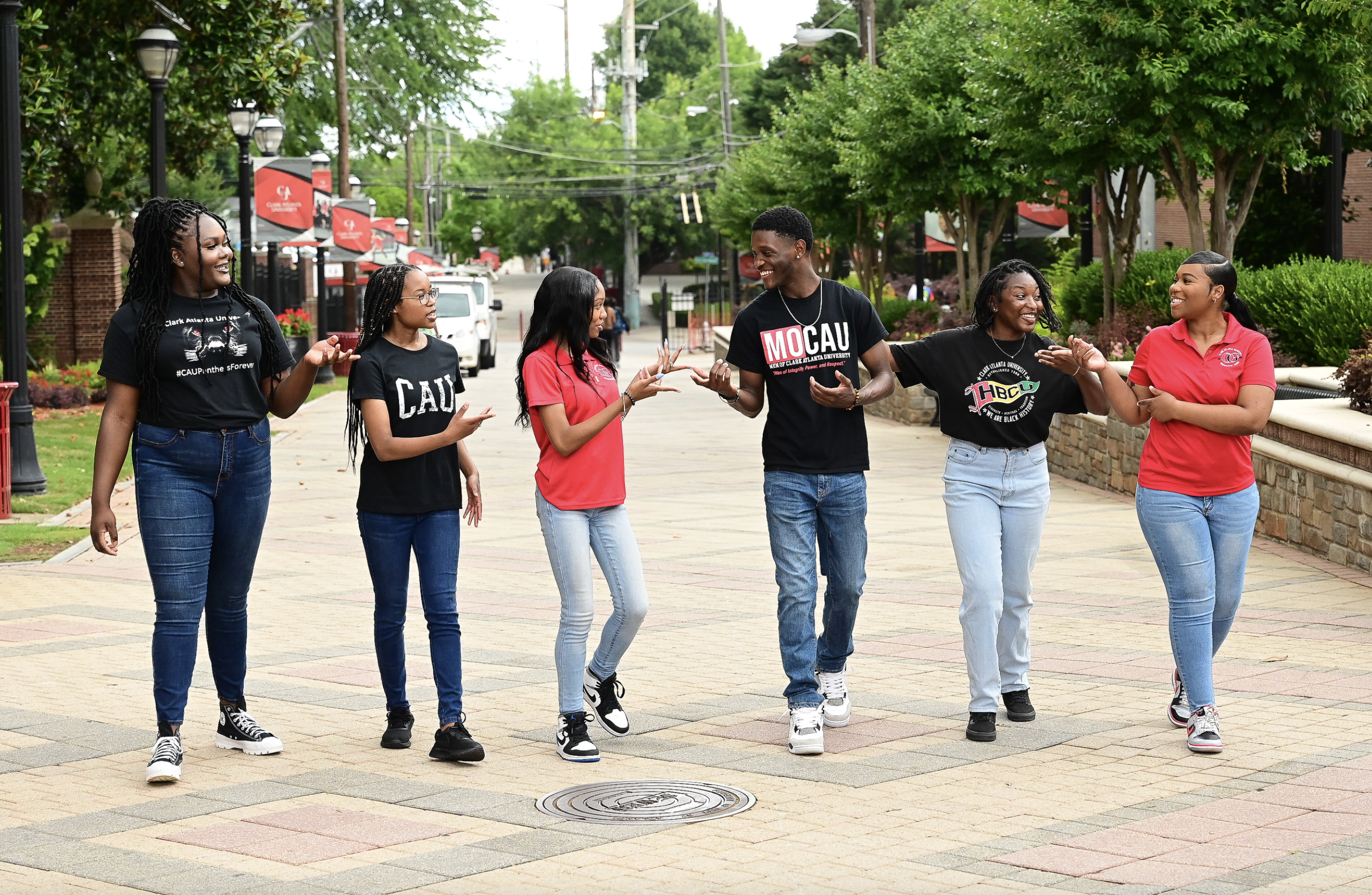 A group of six people walking and talking on a tree-lined path.