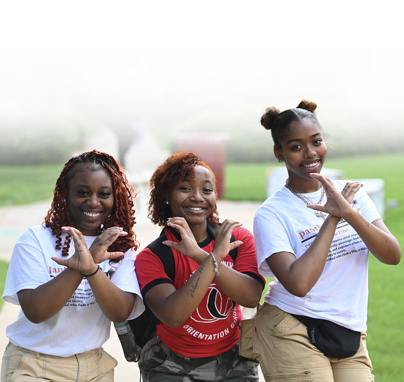 Three smiling women outdoors making hand gestures.