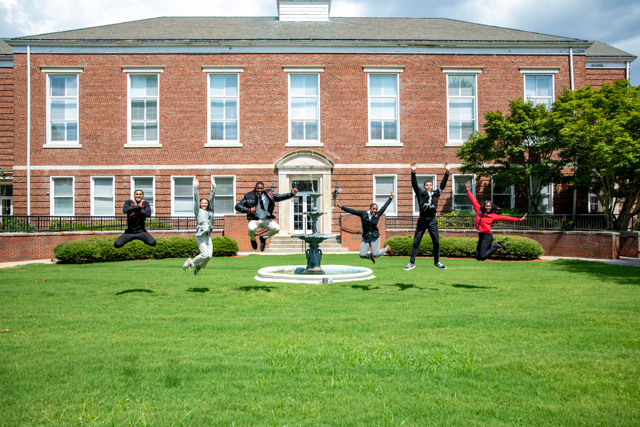 CAU students jumping joyfully on a lawn in front of a red brick building.