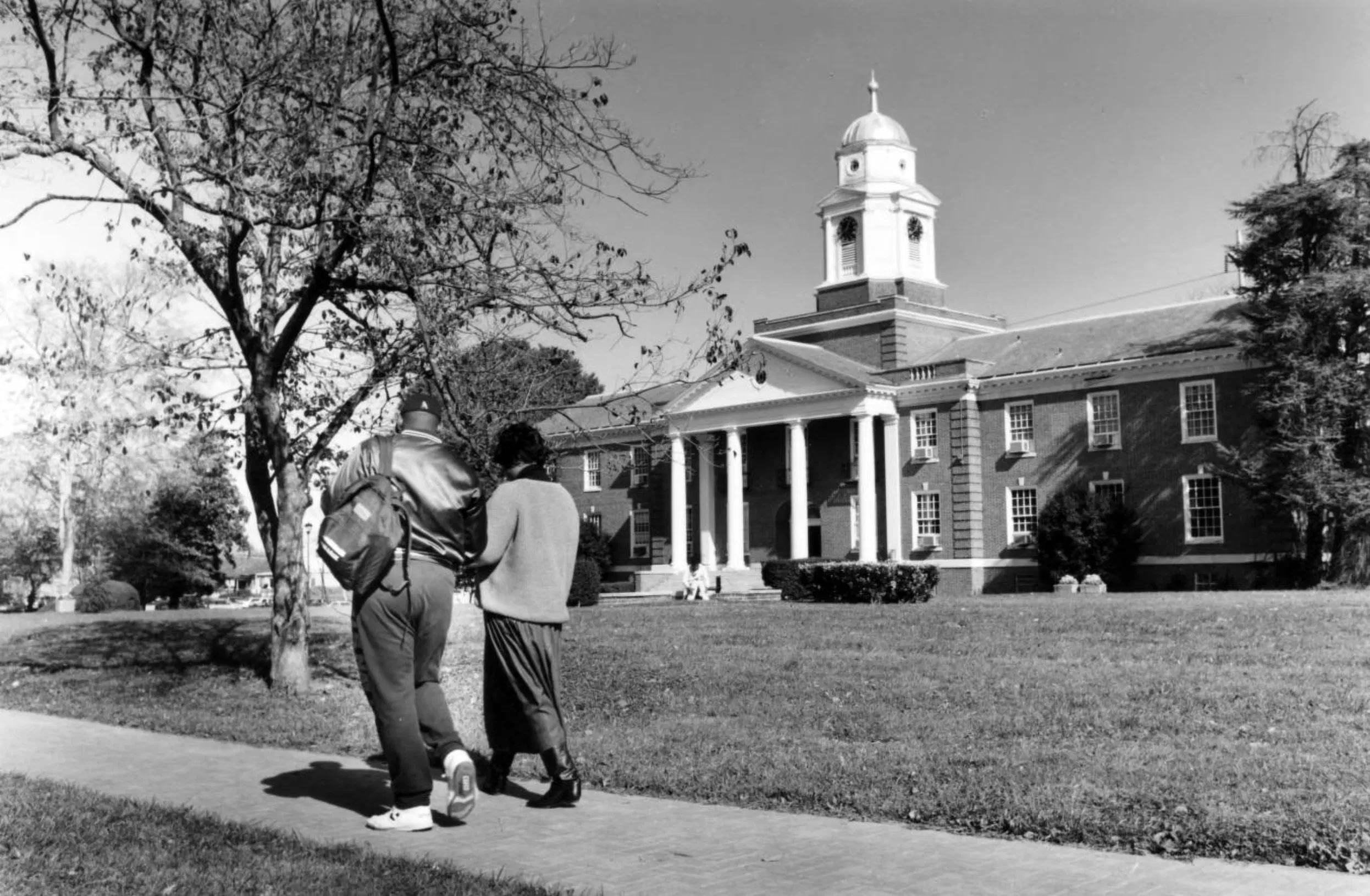 Two people walking on a path, historic building with a clock tower in the background.