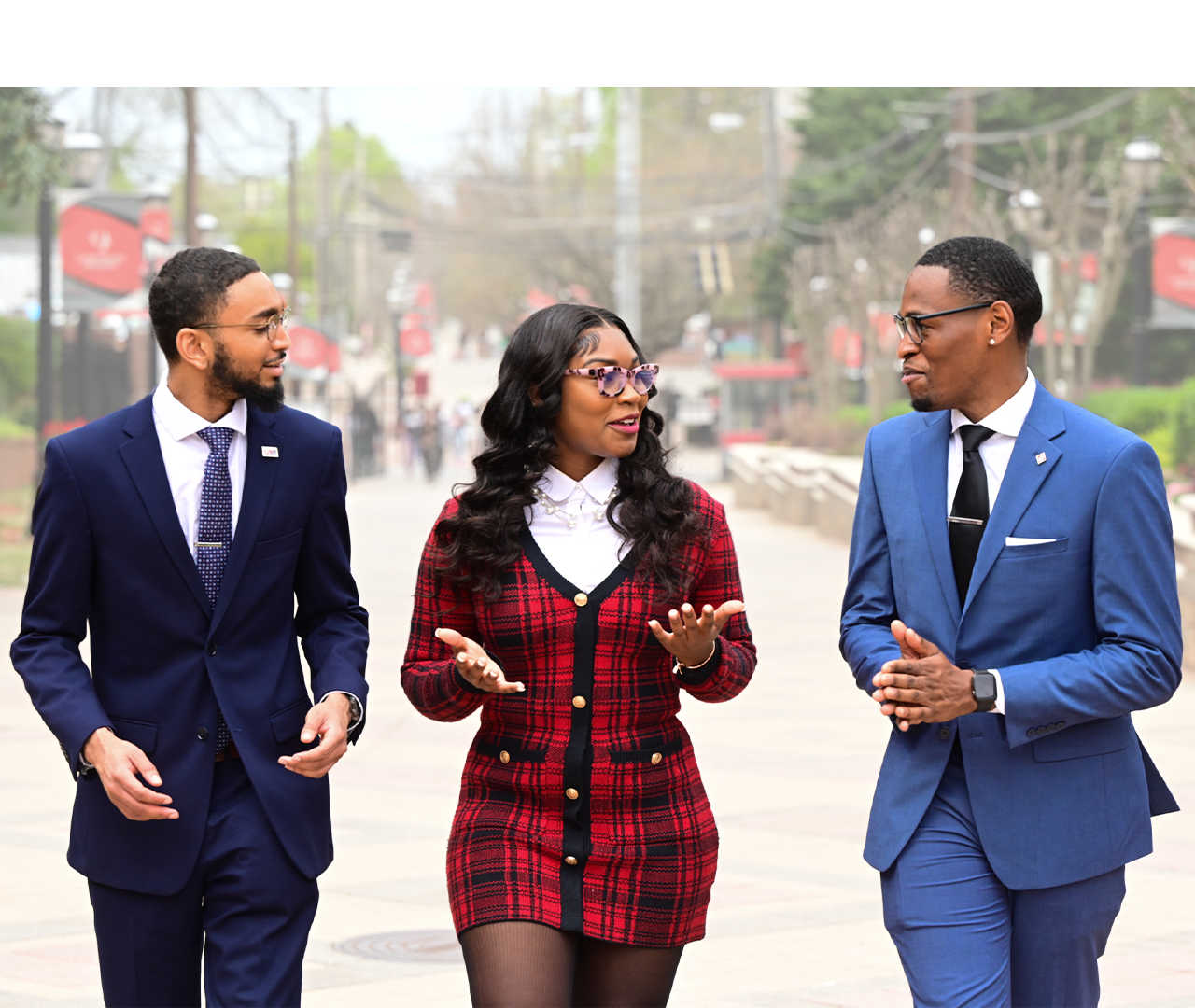 Three people in formal attire walking and talking on a city street.