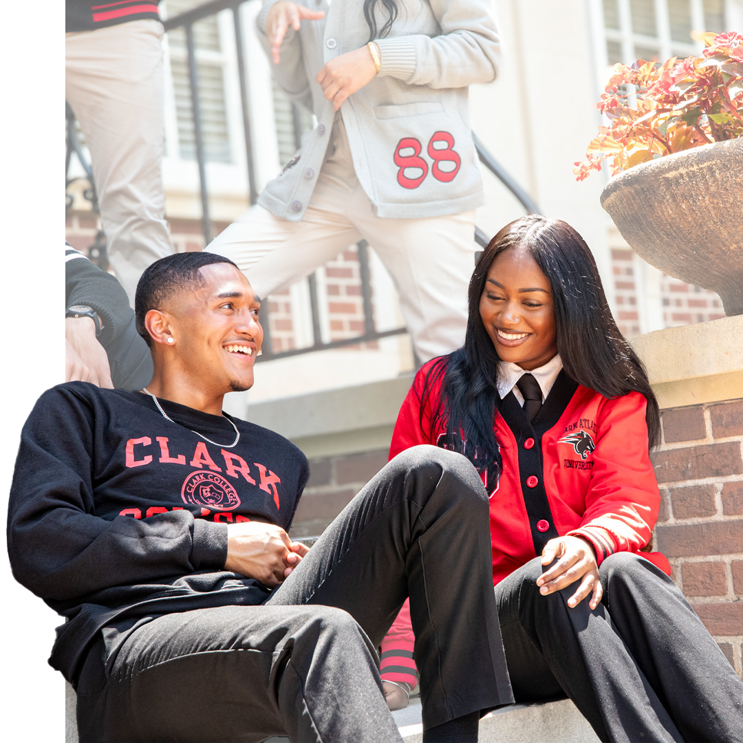 Two students in school apparel smiling and sitting on outdoor steps.