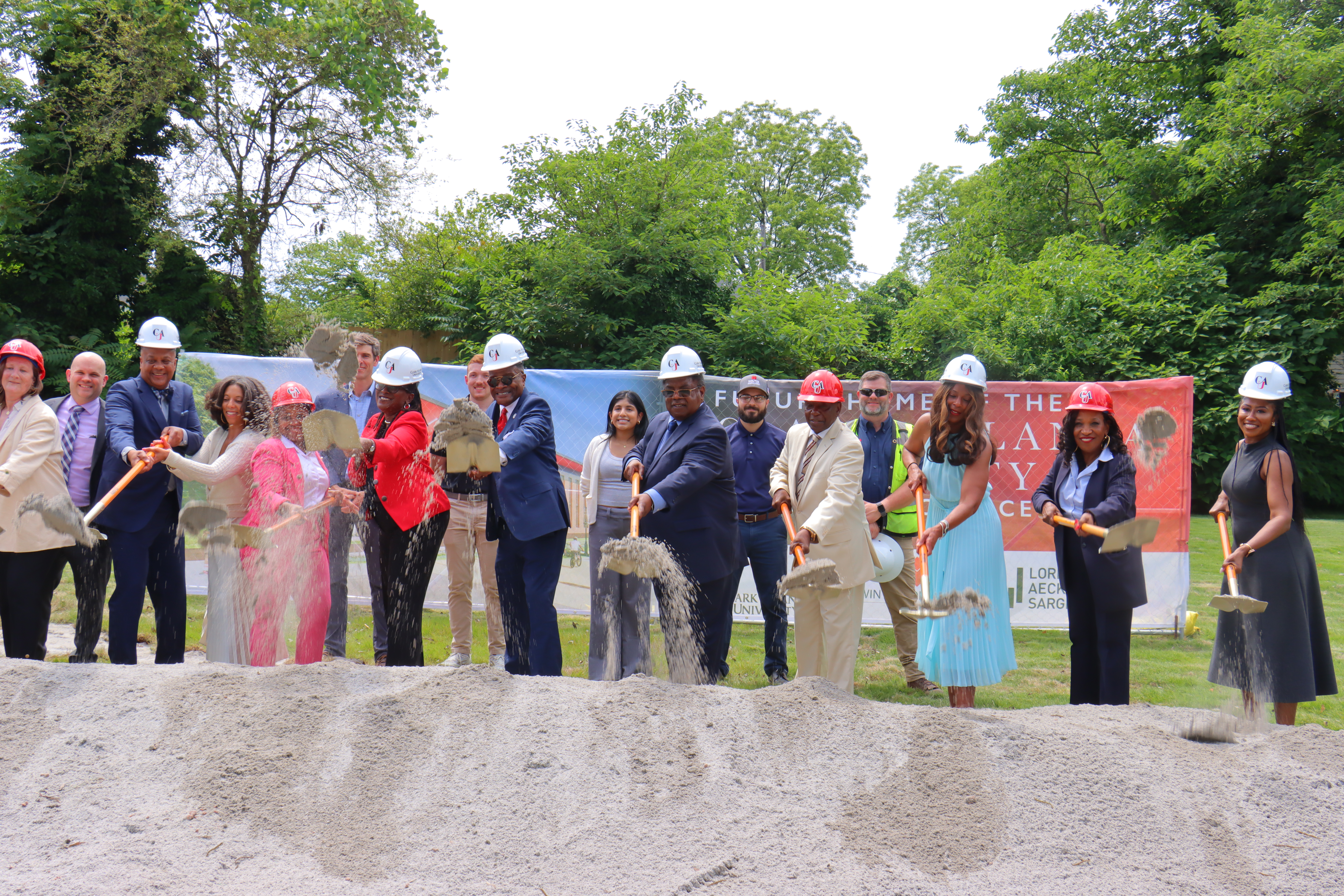 Group of people in hard hats digging with shovels at a groundbreaking ceremony.