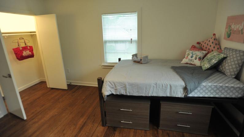 Bedroom with a neatly made bed, wooden floor, and an open closet door.