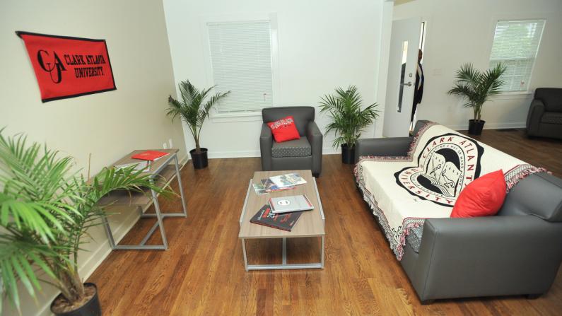 Spacious living room with gray sofa, red pillows, and potted plants.