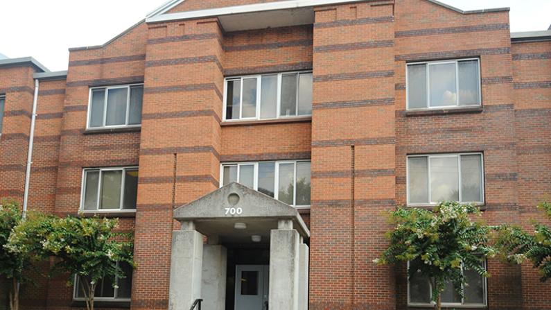 Red brick apartment building with six windows, trees outside.