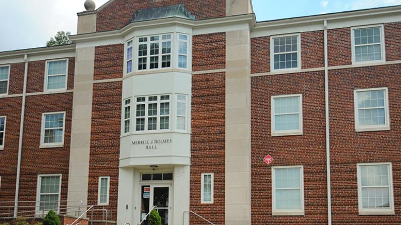 Red brick building with white-trimmed windows and entrance, blue sky background.