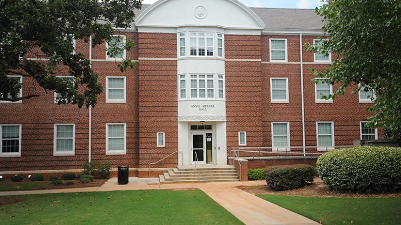 Red brick building with white trim, surrounded by greenery.