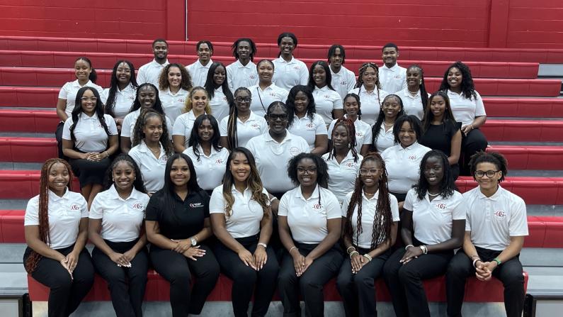 Group of students in uniforms sitting on bleachers, photographed indoors.