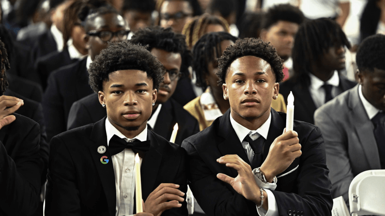 Students in suits holding candles at a ceremony.