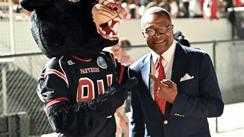 A person in a suit poses with a panther mascot at a crowded sports event.