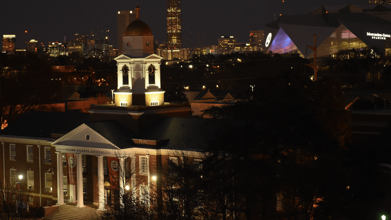 Historic building with a lit domed tower at night, city skyline in the background.