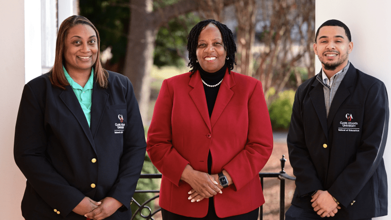 Three people standing outside, two in dark blazers, one in a red blazer, all smiling.