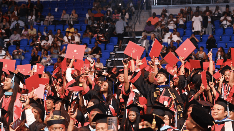 Graduates celebrate, tossing red caps in an indoor arena.