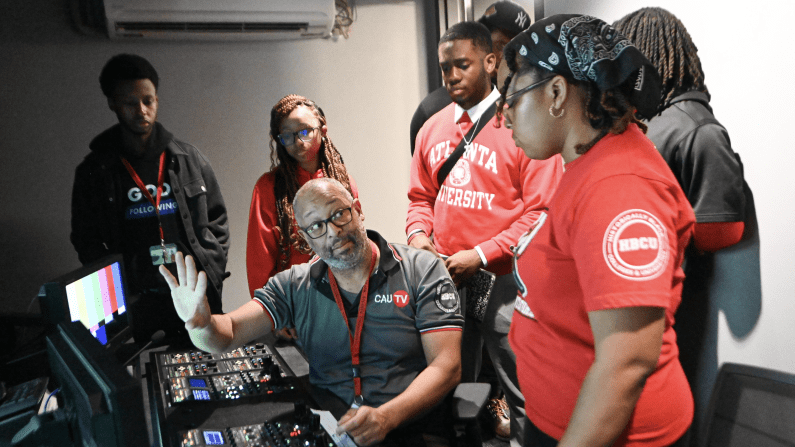 Group of people in a control room, one man explaining equipment.