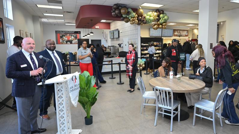 A busy restaurant interior with people listening to a speaker at a podium.