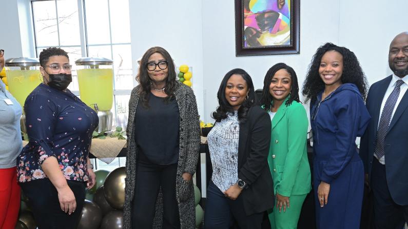 Seven people smiling and posing in a well-lit room.