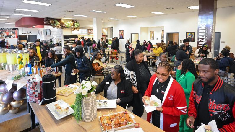 Crowded cafeteria with people in line for food, festive decorations.