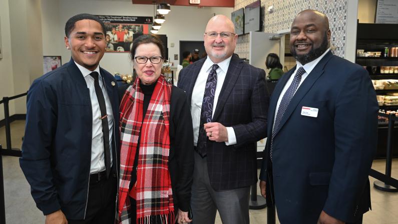 Four people smiling in business attire, standing in a store with a red and white theme.