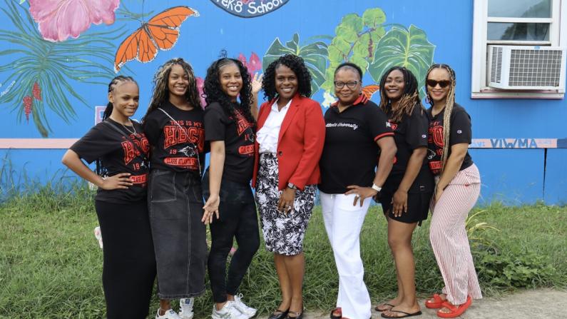 Seven women smiling in front of a colorful mural.