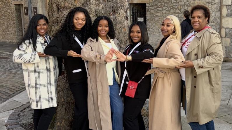 Seven people smiling, holding hands around a large tree in a courtyard in London.