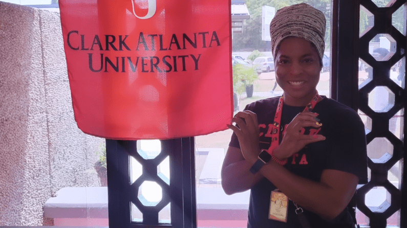 Karen Derr smiling, gesturing under a Clark Atlanta University banner at the W.E.B. Du Bois Memorial Centre