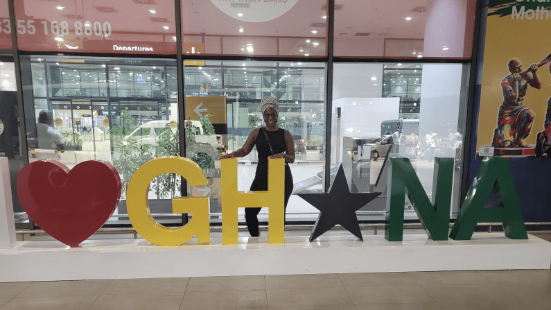 I ❤️ GH★NA sign with Karen Derr standing behind it at Kotoka International Airport.