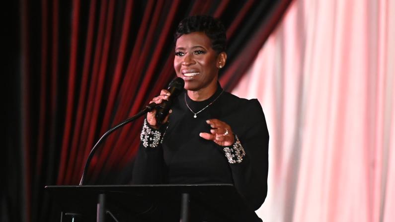 Woman in black speaking at a podium with a microphone.