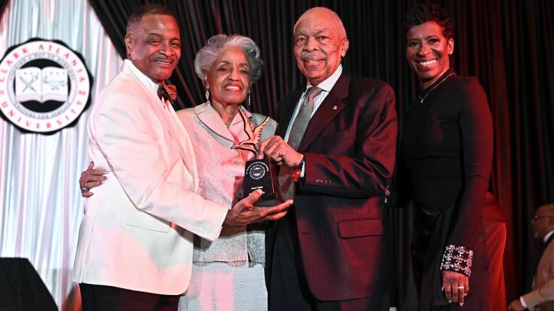 Four people in formal wear smiling at an event, holding an award.