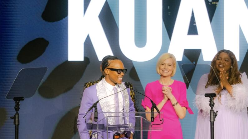 Three people smiling on stage with a cityscape backdrop.