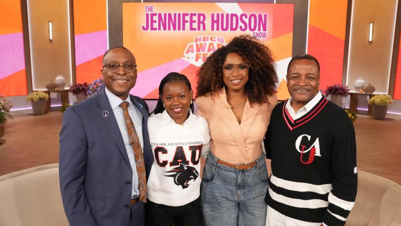 Four people smiling on a talk show set with orange and pink decor.