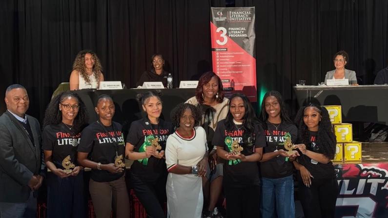 Group photo of smiling people at an event with a table and banners in the background.