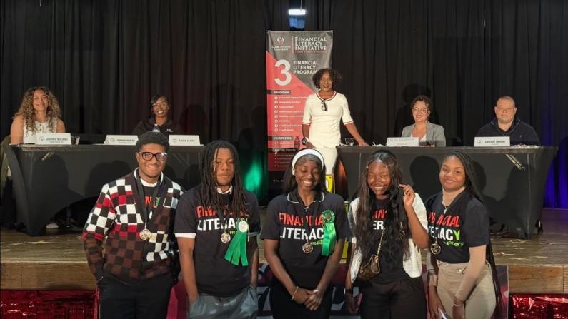 A group of diverse people smiling in front of a panel with banners.