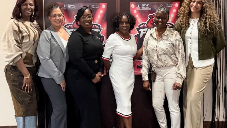 Group of six women standing together and smiling indoors.