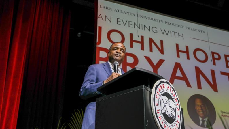 Man speaking at a podium, red curtain, event backdrop.