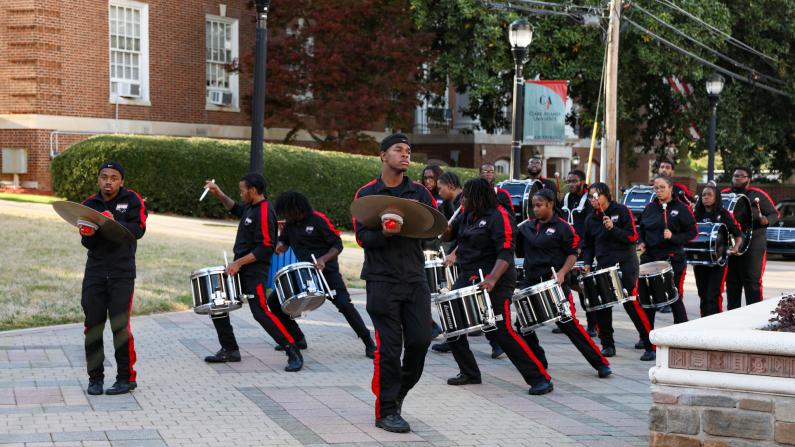 Drumline in black and red uniforms marching on a sidewalk.